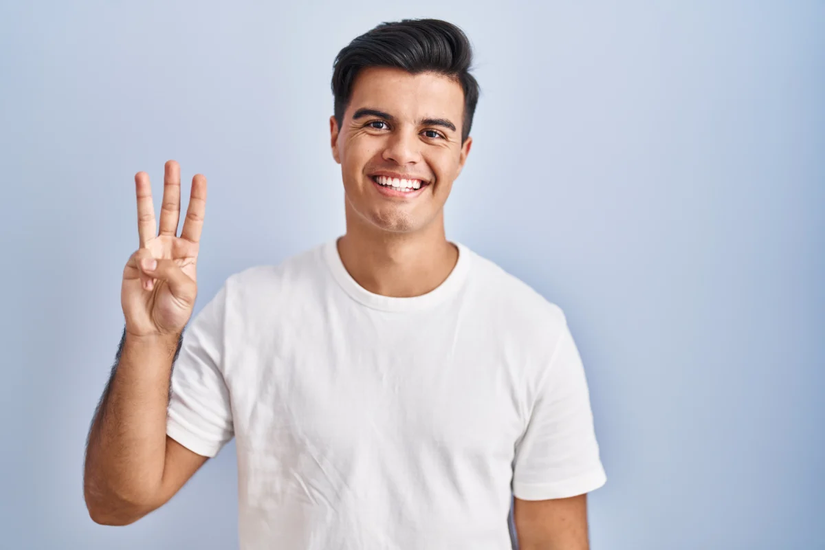 hispanic man standing blue background showing pointing up with fingers number three while smiling confident happy