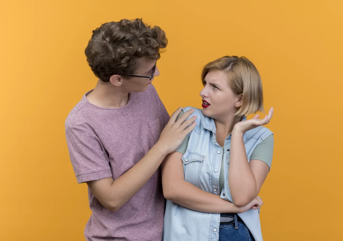 young beautiful couple wearing casual clothes man asking forgiveness displeased woman after fight standing orange wall